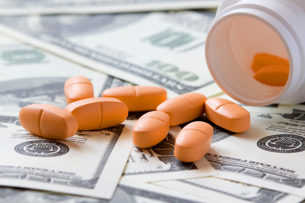 Prescription pills on U.S. dollar bills beside an open pill bottle, illustrating rising medication costs